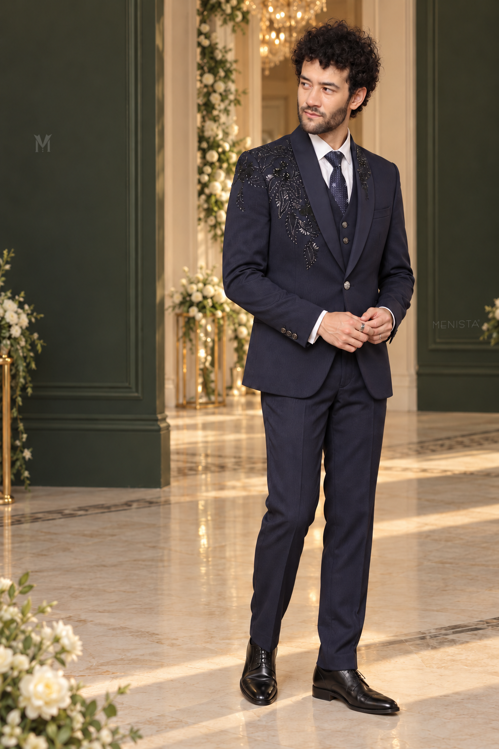 Three-quarter view of Cassian navy floral embroidered tuxedo with one-button jacket fastened over a simple waistcoat and matching trousers.